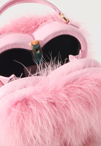 Ροζ τσάντα χειρός με υφή αφράτης γούνας, χρυσό κούμπωμα και στρογγυλεμένη λαβή σε λευκό φόντο.