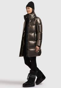 Metallic puffer coat in dark gray with a high collar, side zippers, and large quilted sections. Paired with black snow boots and leggings.