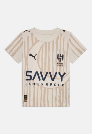 T-shirt beige a maniche corte con righe verticali, caratterizzato da un collo rotondo, logo Puma e le scritte "ALHILAL" e "SAVVY" in blu navy.