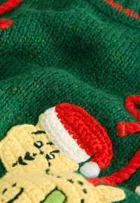 Tissu en maille verte avec une finition texturée, présentant un personnage de dessin animé coloré portant un chapeau de Père Noël rouge et blanc, agrémenté de détails rouges.