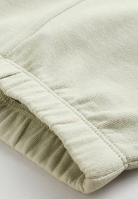 Béžová pletená látka zblízka, ukazující žebrovaný lem a detail hladkého texturovaného rukávu.