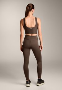 Barna sportmelltartó széles pántokkal és kerek hátrésszel, magas derekú barna leggingsgel párosítva. Mindkettő sima, rugalmas anyagból készült.