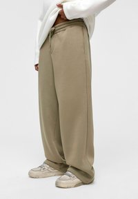 Beige baggy sweatpants met een elastische tailleband en zijzakken, gecombineerd met lichtgekleurde sneakers. Glad, zacht textuur van de stof.