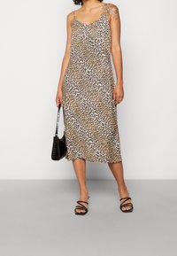 Robe midi à imprimé léopard avec fines bretelles et coupe décontractée, réalisée dans un tissu léger. Sandales noires à lanières et sac à main noir.