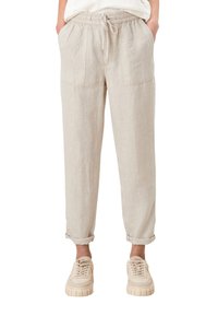 Beige linnebyxor med elastisk midja, framfickor och uppvikta ärmar, kombinerade med ljusbeige sneakers med tjocka sulor.