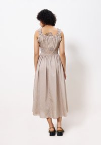 Gestreiftes Midikleid mit gerafften Schulterträgern, tailliertem Schnitt und fließendem Rock. Das Material hat vertikale beige und sanft orangefarbene Streifen.