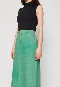 Svart ärmlös topp i kombination med en lång grön denimkjol. Kjolen har en knappstängning, bältesöglor och en strukturerad tyg.