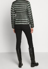 Vadderad olivgrön jacka med kviltat mönster och svarta accenter, tillsammans med åtsittande svarta jeans och knähöga svarta stövlar.