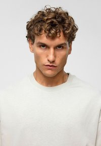 T-shirt en coton gris clair avec un col rond et des manches courtes. Le tissu a une texture lisse et le design est simple et sans ornements.