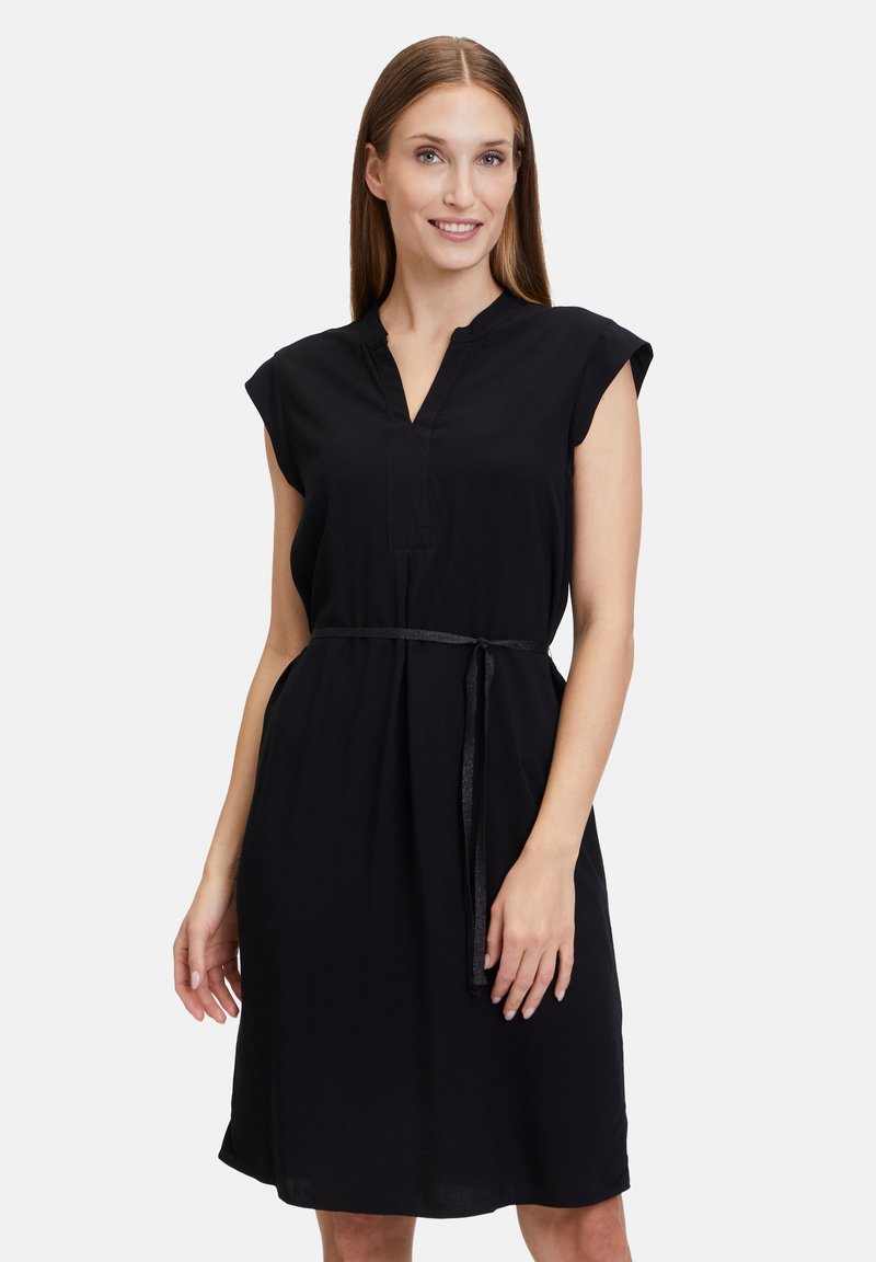 Schwarzes Kleid mit kurzen Ärmeln, V-Ausschnitt und einem abnehmbaren Bindegürtel. Hergestellt aus leichtem Material mit glatter Textur. Schlicht, knielang.