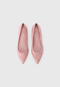 Ροζ μπαλαρίνες από δερμάτινο λουστρίνι με μυτερή μύτη και διακόσμηση σε σχήμα καρδιάς στο παπουτσάκι. Ομαλή υφή με διακριτική λάμψη. Χρυσό λογότυπο στο εσωτερικό.