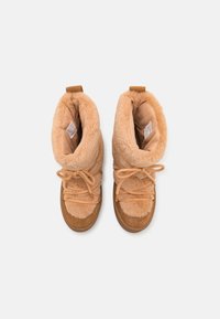 Bottes ankle en fourrure marron avec des garnitures en suède beige. Dotées d'un système de laçage et d'une texture douce et moelleuse. Design bi-ton avec une forme de bout arrondi.