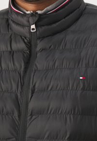 Sort dunjakke med høj krave og grå indvendig. Lynlås foran og lille logo med røde, hvide og blå accenter på brystet.