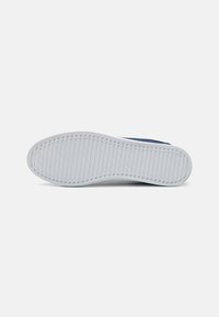 Fehér gumi sneaker talp, textúrált tapadási mintával. Sötétkék felsőrésze sima anyagból készült, és kerek orrú kialakítással rendelkezik.