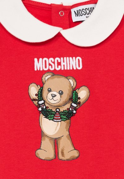 Červený odev s bielym golierom typu Peter Pan, na ktorom sa nachádza usmievajúca sa medvedík s vianočným vencom a nápisom "MOSCHINO" nad ním.