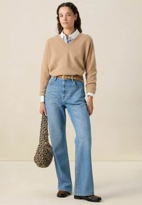 Pull en tricot beige, jean taille haute bleu clair, sac à imprimé léopard, chaussures noires. Texture douce, coupe décontractée, taille bien définie.