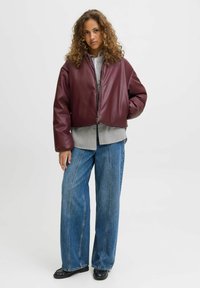 Burgundowa skórzana kurtka w wersji cropped z przednim zamkiem, noszona na czarno-białą koszulę w kratę, w połączeniu z szerokimi niebieskimi dżinsami.