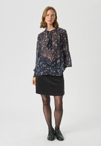Bluză florală de culoare bleumarin cu accente roz, decorată cu volane și mâneci lungi, asortată cu o fustă din catifea neagră și loafers negri.