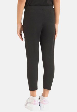 Leggings neri aderenti realizzati in tessuto elasticizzato, con una texture liscia e lunghezza a metà polpaccio. Abbinati a sneakers bianche.