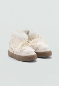 Bijele čizme do gležnja obložene umjetnim krznom s bež naglascima, ravnim smeškim gumiranim potplatima i kremastim vezicama. Imaju zatvarač za jednostavno obuvanje.