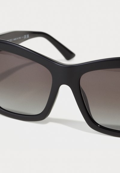 Lunettes de soleil noires avec une monture brillante, grandes lentilles carrées dégradées du noir au gris clair, et branches noires lisses.