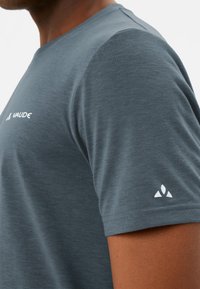 Grijze T-shirt met korte mouwen en een ronde hals. Voorzien van een witte logo op de voorkant en een klein embleem op de linkermouw. Zachte, gestructureerde stof.