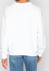 Sweatshirt blanc avec une coupe décontractée, des manches longues et un col rond, associé à un jean en denim bleu clair. Texture lisse.