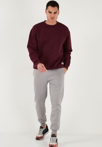 Bordeaux sweatshirt met een ronde hals, gecombineerd met grijze sweatpants en multicolore sneakers; heeft ribbels aan de manchetten en de onderrand.