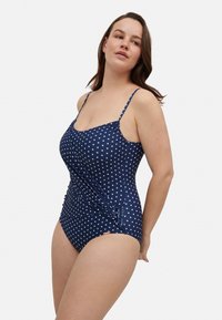 Bañador de una pieza azul marino con lunares blancos. Presenta tirantes delgados ajustables y un detalle lateral fruncido para mayor textura.