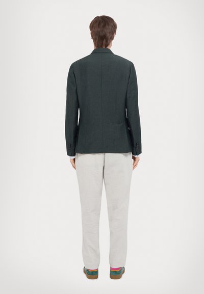 Blazer vert foncé avec une coupe ajustée, une fente au dos et deux boutons. Associé à un pantalon gris clair et des chaussures multicolores.