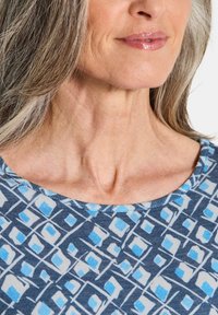 Blau-weiß gemusterter Stoff mit Rautenformen; runder Ausschnitt; glatte Textur; dezenter Glanz. Nahaufnahme von Kragen und Nackenbereich.
