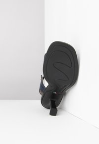 Denim sandal med en sort gummiydersål, firkantet hæl og beige detaljer. Har en tekstureret sål og branddetalje på sålen.