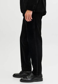 Čierne zamatové nohavice so rovný strihom, s hladkou textúrou a jemnými bočnými pruhmi. Skombinované s čiernymi koženými poltopánkami.