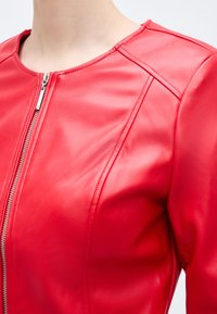 Κοντινό πλάνο ενός ατόμου που φοράει φωτεινό κόκκινο δερμάτινο μπουφάν με ασημένιο φερμουάρ μπροστά και εμφανείς ραφές στους ώμους και το στήθος.