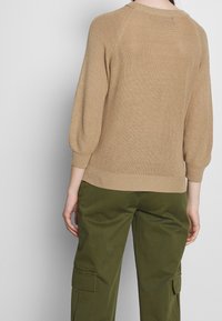 Beżowy sweter dzianinowy z rękawami 3/4 w kształcie bufka i prążkowanym dołem, połączony z oliwkowymi spodniami cargo. Teksturowany materiał.