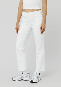 Jeans évasés blancs en denim, avec une taille mi-haute, des poches avant et un léger effilochage à l'ourlet. Assortis à des baskets blanches.