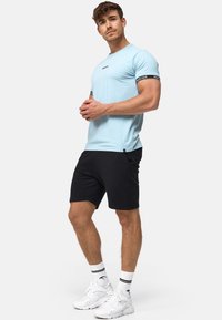 Lys blå kortermet skjorte med en svart stripe som har tekst, kombinert med svarte shorts og hvite joggesko. Enkel design og pustende materiale.