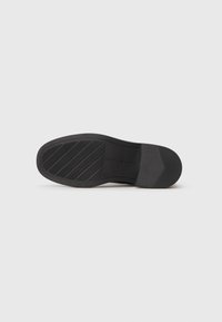 Suela de zapato negra con agarre texturizado y marca, mostrada plana sobre un fondo blanco.