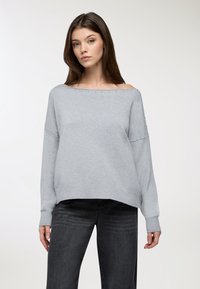 Maglione grigio chiaro a spalle scoperte con polsini e orlo a costine, caratterizzato da rivetti decorativi lungo il collo. Tessuto morbido e vestibilità rilassata.