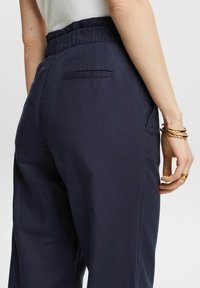 Mörkblå bomullsbyxor med avslappnad passform, elastisk midja och en bakficka. Slät textur med enkla design detaljer.