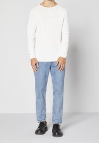 Vit långärmad skjorta med en texturerad yta, i kombination med ljusblå jeans och svarta snörskor.