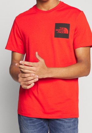 Rød T-shirt med korte ærmer og et sort firkantet logo på venstre bryst. Fremstillet af blødt stof med klassisk rund hals.