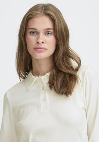 Kerman ribbed pitkähihaine polo-paita, jossa on kauluspaita ja kolme napin aukkoa. Sujuva tekstuuri, jossa on hillityt pystysuorat viivat.
