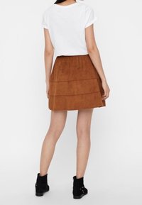 Brauner Wildlederrock mit drei horizontalen Schichten, kombiniert mit einem weißen Oberteil mit hochgerollten Ärmeln und schwarzen Knöchelstiefeln. Glatte Textur.