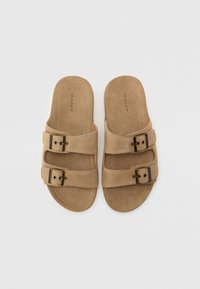 Sandales en suede marron avec deux larges brides réglables, ornées de boucles métalliques et d'une semelle plate. Logo de la marque estampé sur la semelle intérieure.