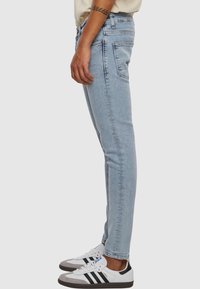 Light blue denim jeans with a slim fit, featuring a mid-rise waist, classic five-pocket design, and subtle fading. Paired with white sneakers.