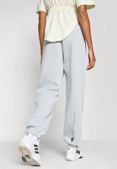 Light grey sweatpants with elastic cuffs and logo detail on the side, paired with a loose-fitting yellow top. White sneakers with black accents.