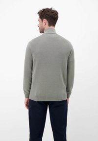 Hellgrüner, gestrickter Pullover mit hohem Kragen, strukturiertem Muster und gerippten Bündchen, getragen über einer dunklen Hose. Rückansicht angezeigt.