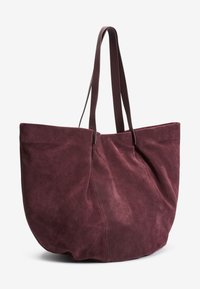 Bordeaux ruskind tote taske med to lange håndtag, der har en rund form og glat tekstur, designet til rummelig opbevaring.
