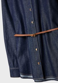 Dunkelblaus Denimhemd mit goldenen Knopfverschlüssen, das einen braunen Gürtelakzent und kontrastierende Nähte entlang dem Saum und den Manschetten aufweist.